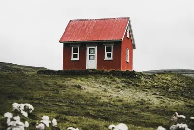 Litet rött hus med rött plåttak på en grön kulle